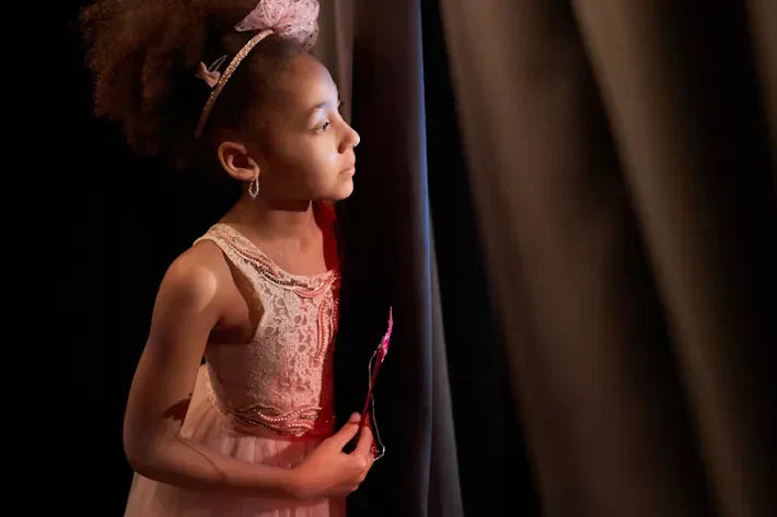 Young girl in a costume looking around curtain on stage.
